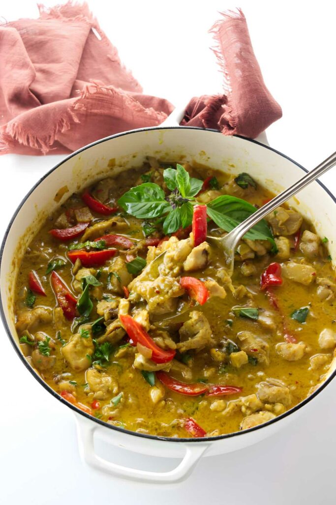 White pot of yellow Thai curry with chicken, peppers, and basil.