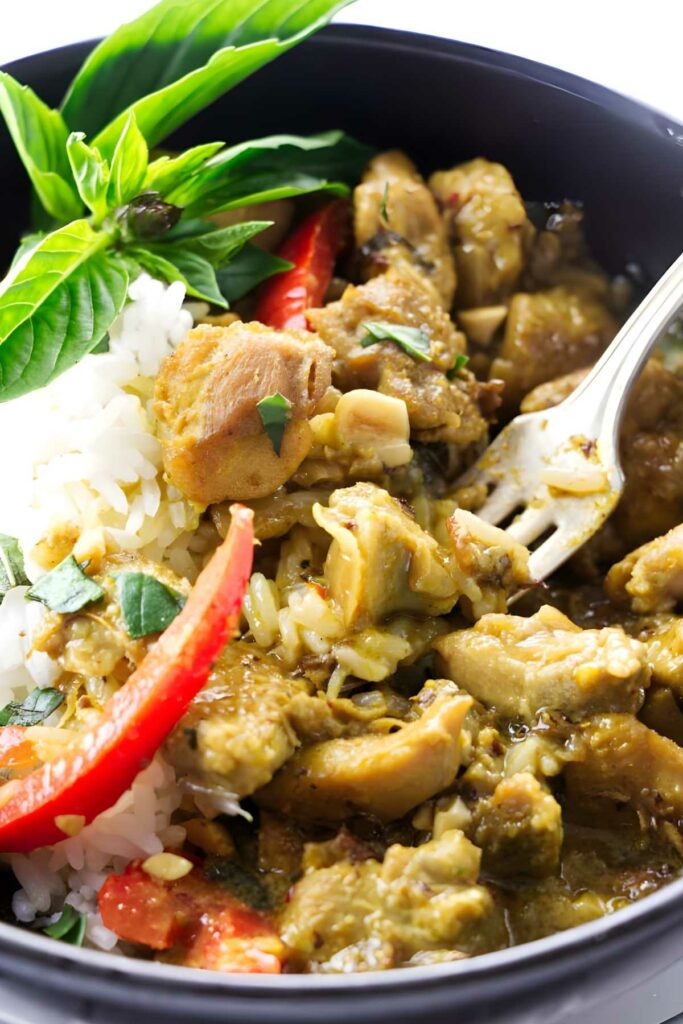 Close-up of yellow curry chicken, rice, red pepper, basil in a bowl.