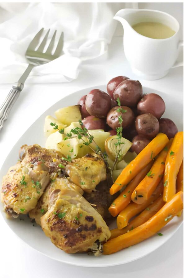Slow cooker chicken with glazed carrots, red potatoes, and onions on a white plate.