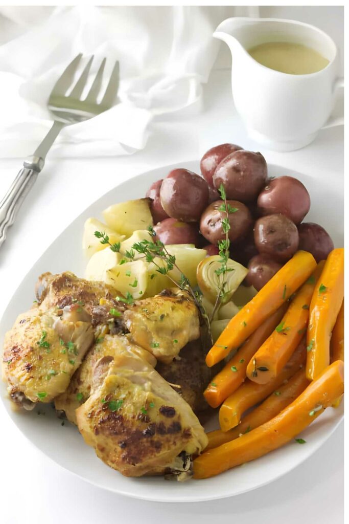 Slow cooker chicken with glazed carrots, red potatoes, and onions on a white plate.