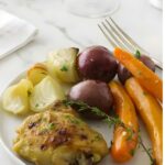 Crockpot chicken with carrots, potatoes, onion, and thyme on a white plate.