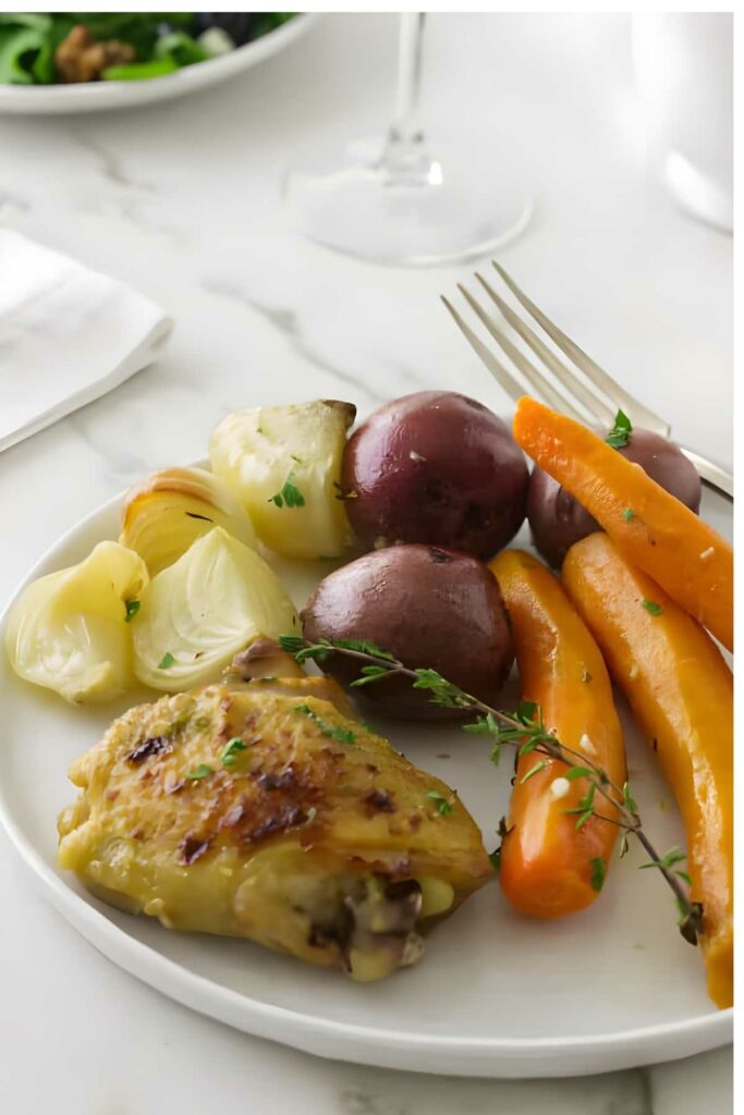 Crockpot chicken with carrots, potatoes, onion, and thyme on a white plate.