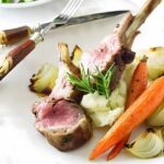 Two lamb chops on mashed potatoes with roasted vegetables and rosemary garnish.
