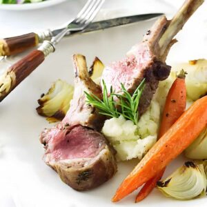 Two lamb chops on mashed potatoes with roasted vegetables and rosemary garnish.