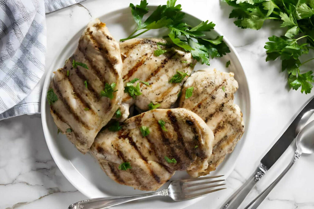 Four chicken breasts on a plate with grill marks.