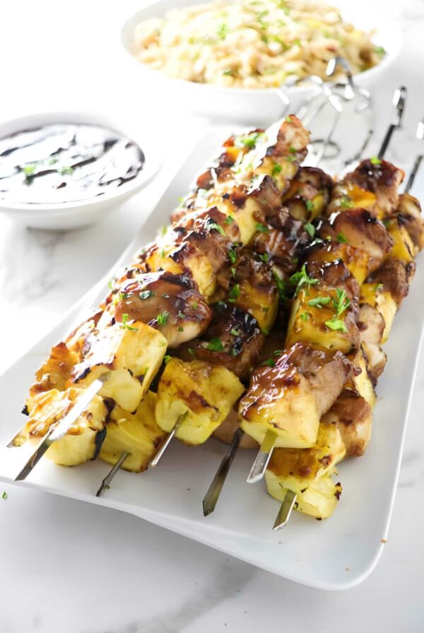 Grilled chicken and pineapple skewers with herbs on a white plate.