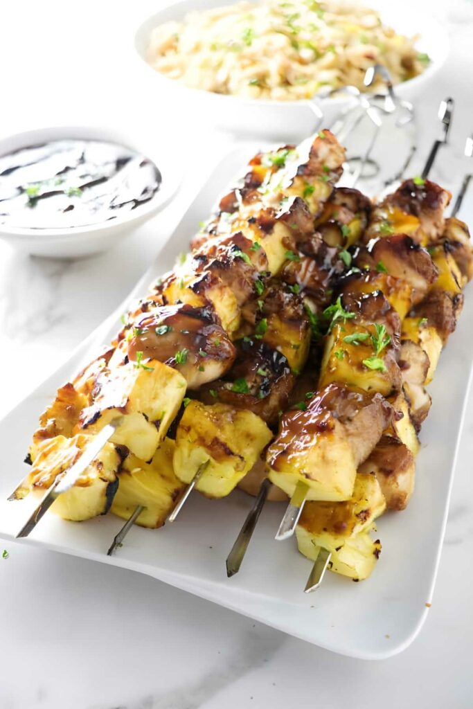 Grilled chicken and pineapple skewers with herbs on a white plate.