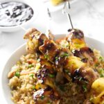 Grilled chicken and pineapple skewers over fried rice in a white bowl.