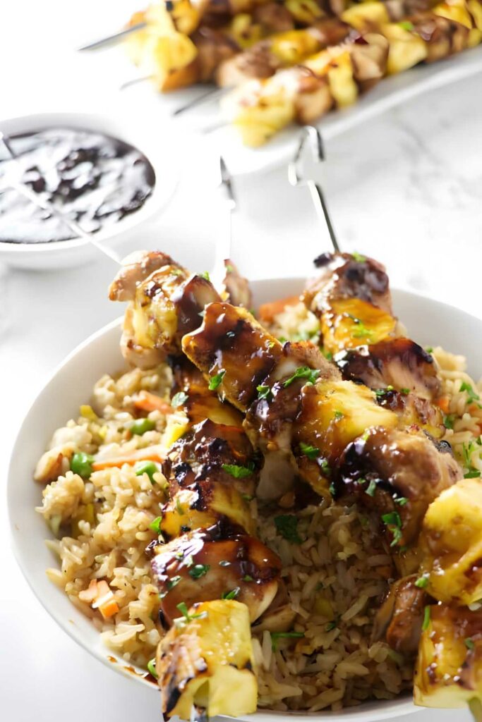 Grilled chicken and pineapple skewers over fried rice in a white bowl.