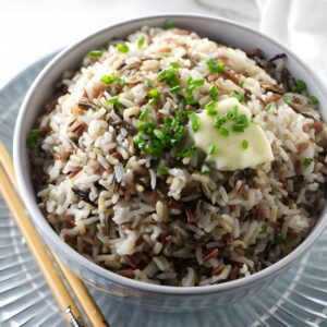 Bowl of mixed rice with butter and chives, chopsticks beside, white cloth background.