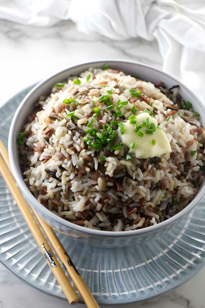 Bowl of royal blend rice with butter and chives, chopsticks beside, white cloth background.