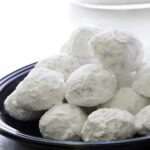 Round cookies covered in powdered sugar on a black plate.