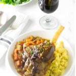 Braised lamb osso buco with carrots, and mashed potatoes with red wine on table.