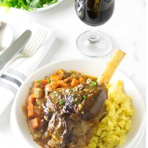 Braised lamb shank, carrots, and mashed potatoes with red wine on table.