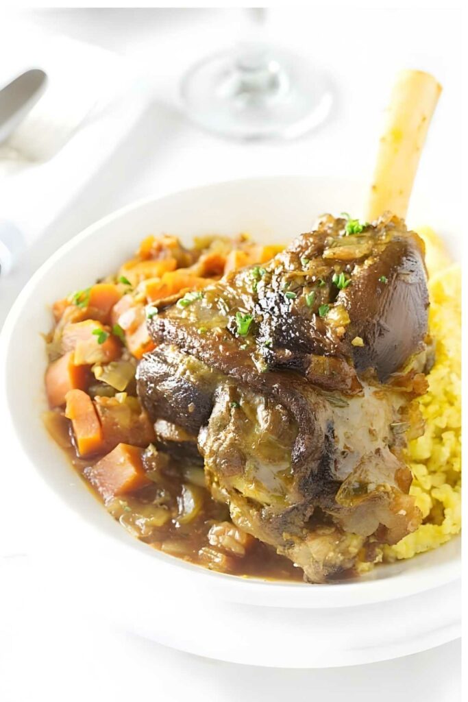 Braised lamb shank on couscous with herbs in a white bowl, vegetable stew.