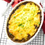 Casserole with melted cheese and herbs on cooling rack, beside spoon.