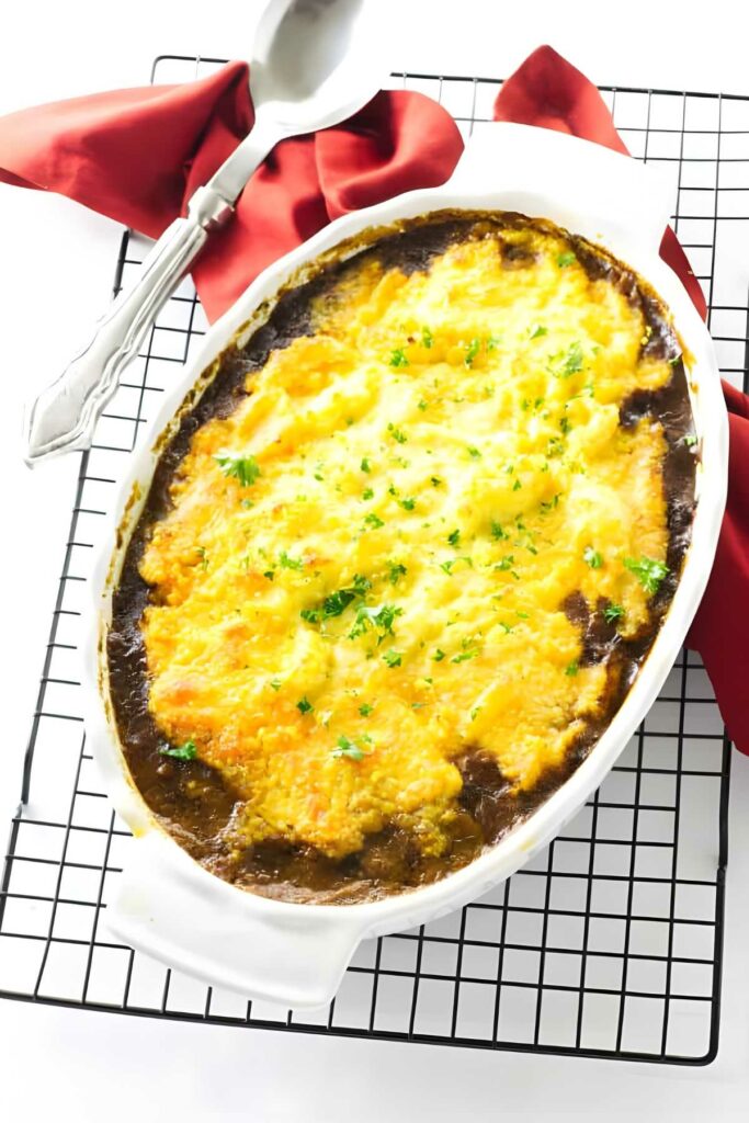 Casserole with melted cheese and herbs on cooling rack, beside spoon.