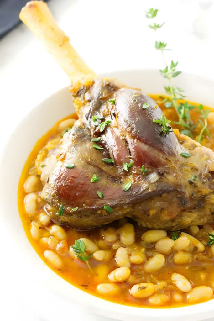 Lamb cassoulet with herbs atop white beans in sauce, in a white bowl.