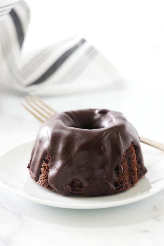 A mini bundt cake on a plate with chocolate glaze on top.