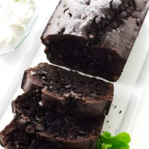 Sliced chocolate bread on a white plate with mint leaves and whipped cream.