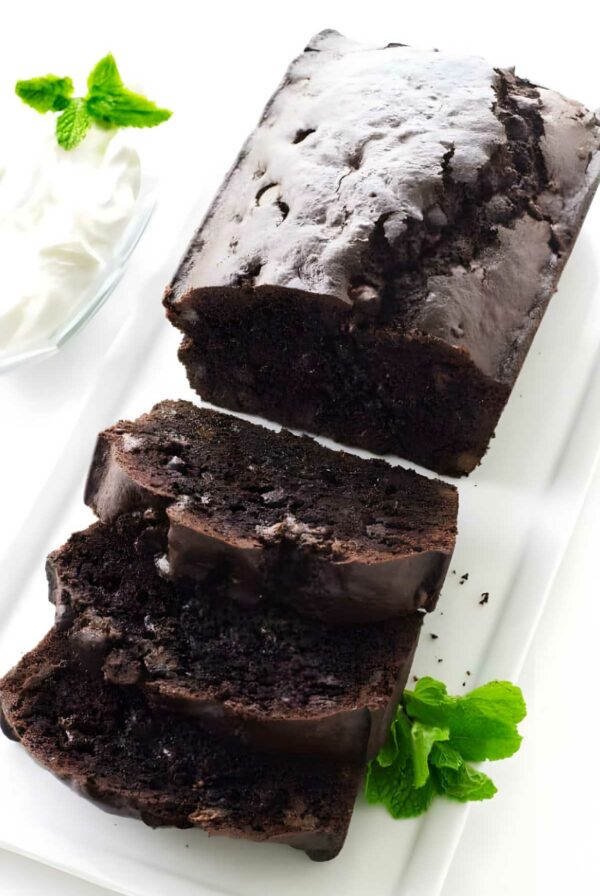 Sliced chocolate bread on a white plate with mint leaves and whipped cream.