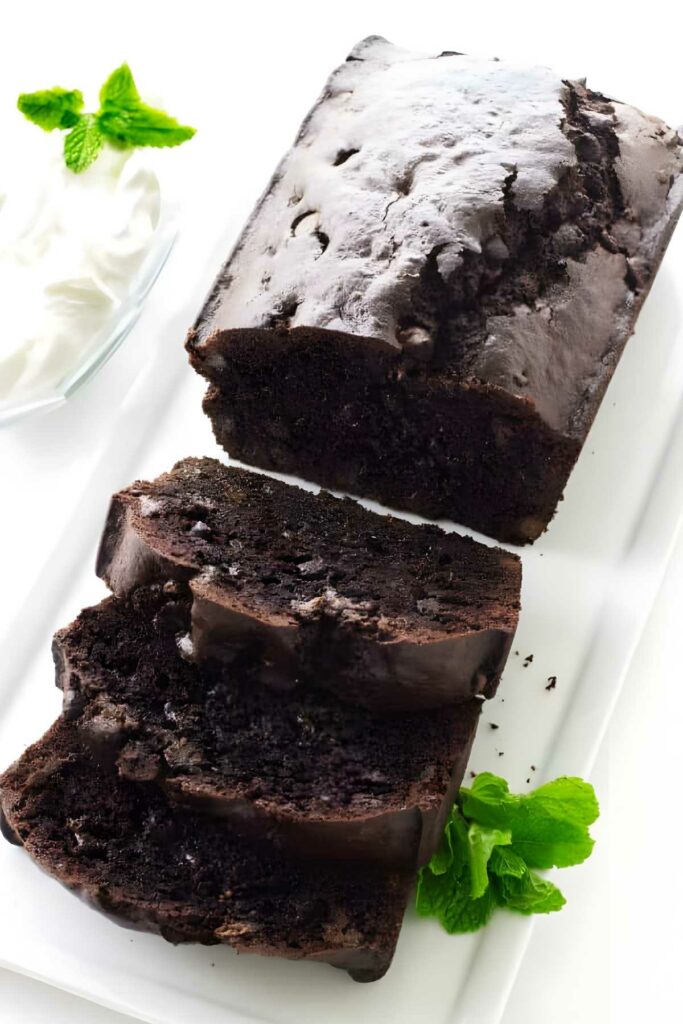 Sliced chocolate bread on a white plate with mint leaves and whipped cream.