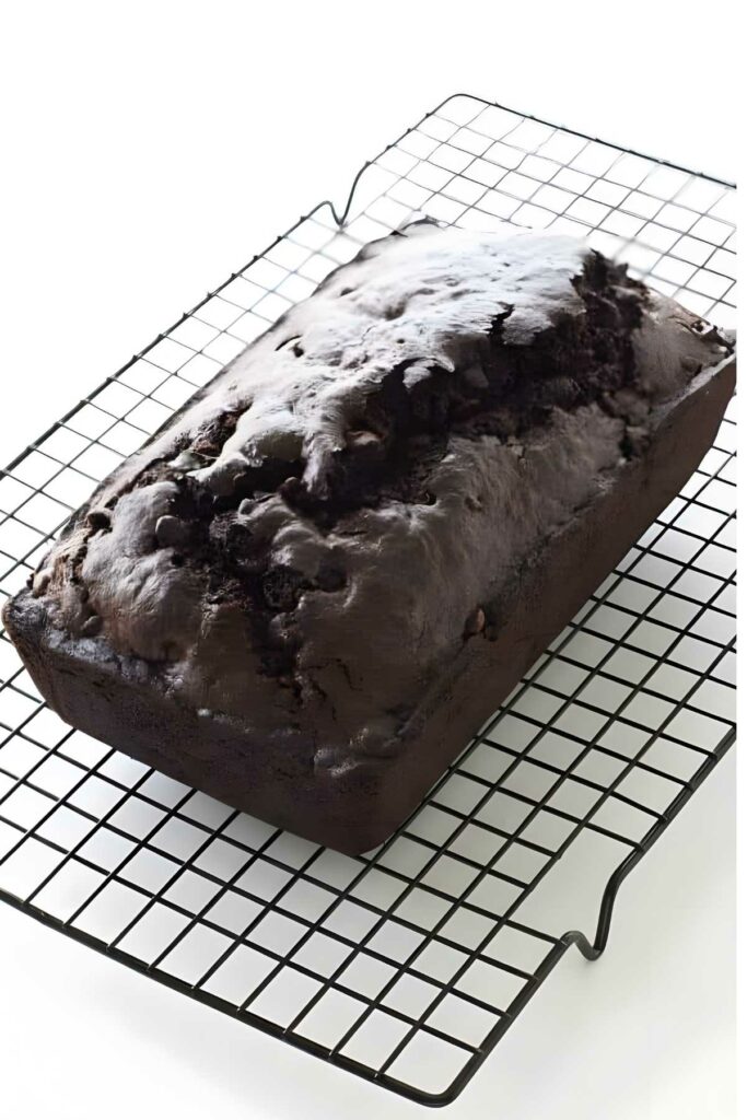 Chocolate loaf cake with cracked top on cooling rack, white background.