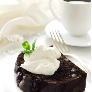 Chocolate cake slice with whipped cream and mint on a plate, coffee nearby.