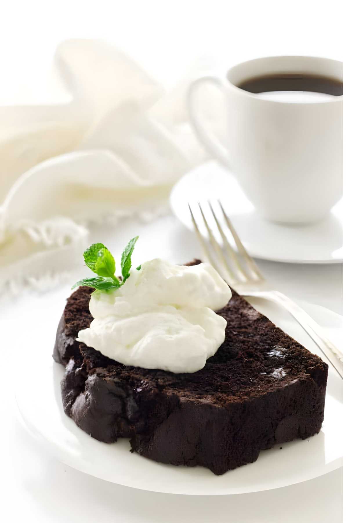 Chocolate mint cake slice with whipped cream and mint on a plate, coffee nearby.