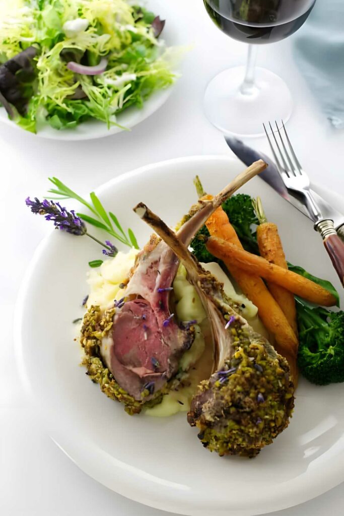 Nut crusted rack of lamb with vegetables, mashed potatoes, salad, and red wine.