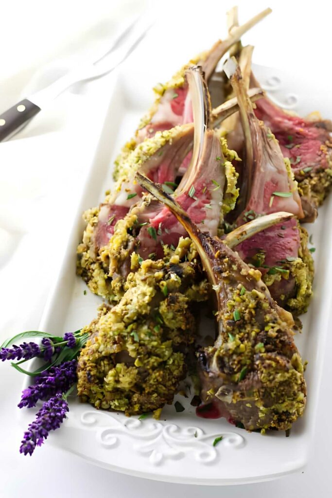 Pistachio crusted rack of lamb on white platter, garnished with herbs.