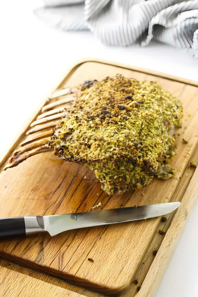 Rack of lamb with golden crust on cutting board beside sharp knife.