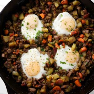 Skillet hash with potatoes, carrots, meat, and sunny-side-up eggs on top.