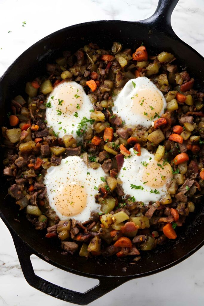 Skillet hash with potatoes, carrots, meat, and sunny-side-up eggs on top.