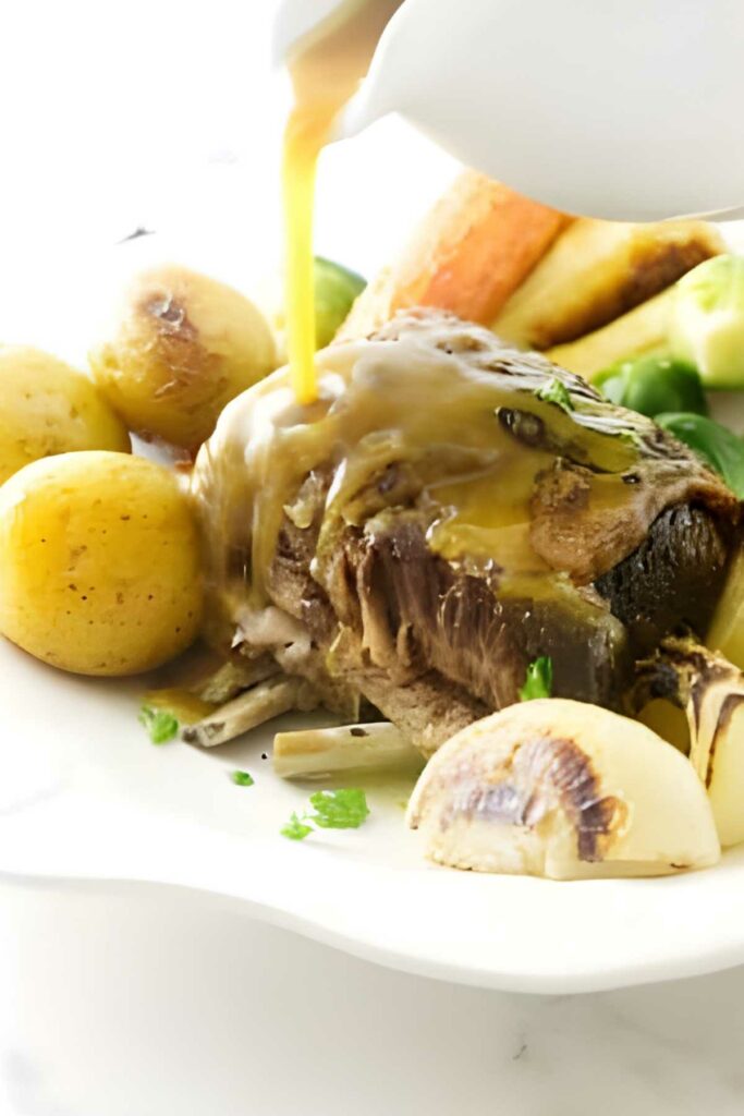 Pot roast with potatoes, carrots, onions, and gravy being poured from a white boat.