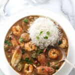 Shrimp and sausage gumbo with rice, garnished with herbs on a white plate.