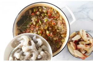 Pot of gumbo with vegetables, two bowls of shrimp and fish on marble.