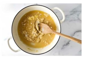 White pot with light brown roux and wooden spoon on marble surface.