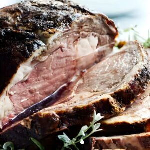 Sliced prime rib beef with herbs, greens, and broccoli in background.
