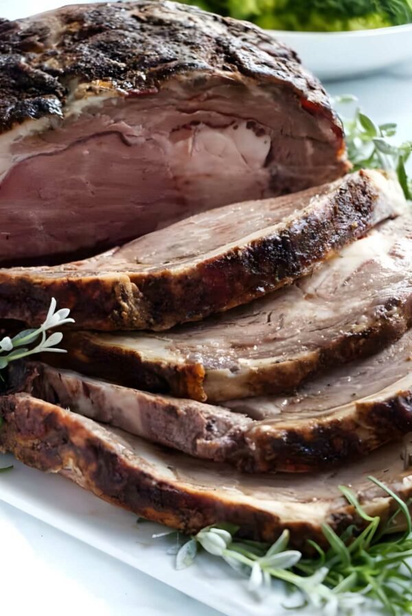 Sliced prime rib beef and herbs on a cutting board with unsliced portion.