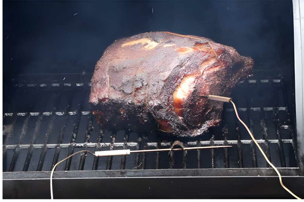 Seasoned meat with temperature probes grilling, smoke rising inside the grill.