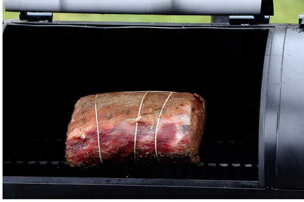 Seasoned prime rib tied with twine sits in an open smoker grill.