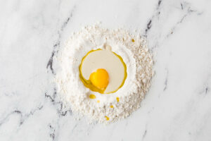 Flour on a counter with egg yolk and oil in the center.