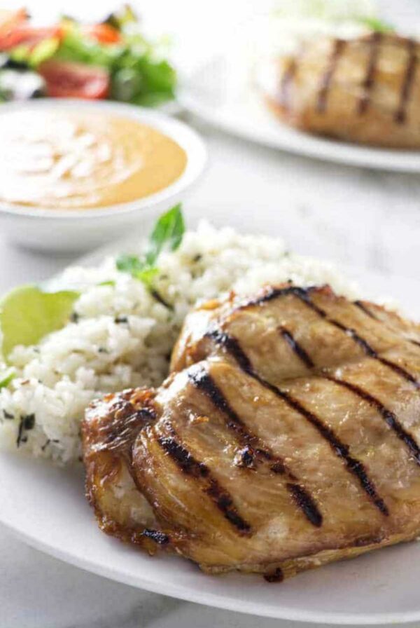 Grilled chicken breast with rice and lime on a plate, salad behind.