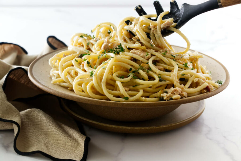 A spoon lifting noodles from a bowl of tuna pasta.