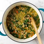A soup ladle scooping up brothy white bean soup with spinach and chicken.