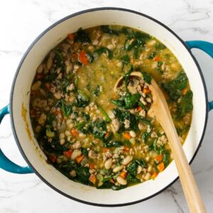 A soup ladle scooping up brothy white bean soup with spinach and chicken.