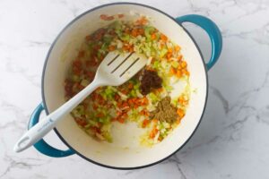 Adding spices to the softened veggies in a Dutch oven.
