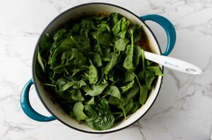 Adding spinach to the pot of soup.