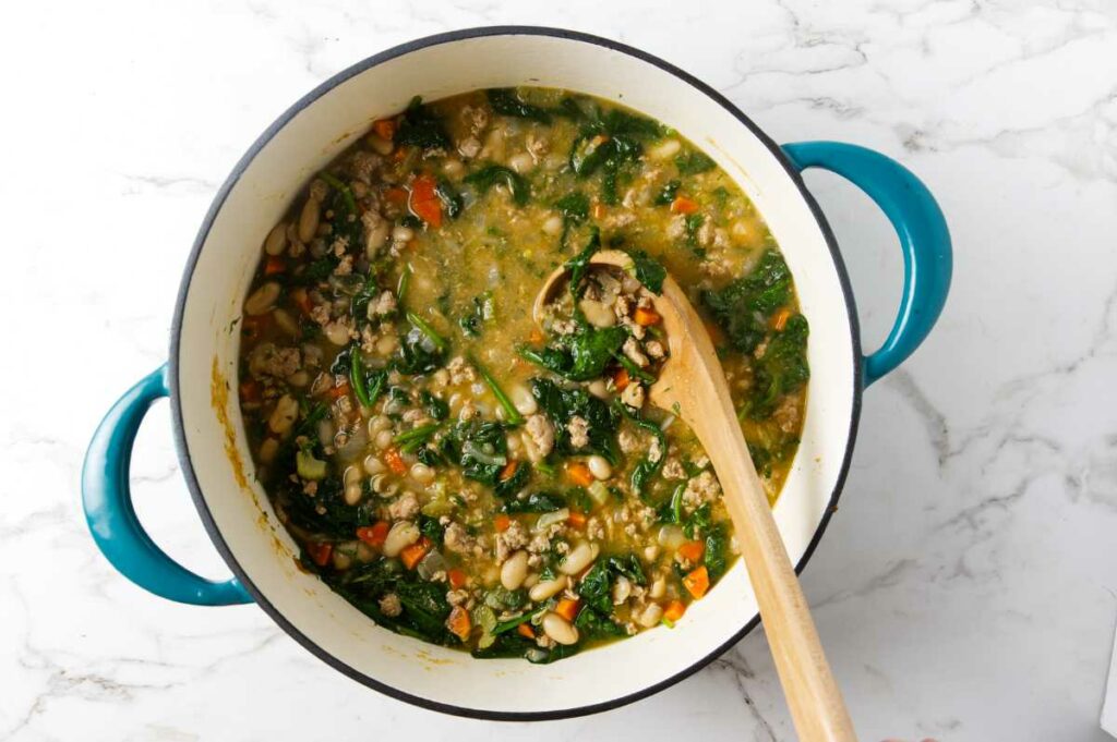 A wooding ladle in a pot of bean soup with spinach.